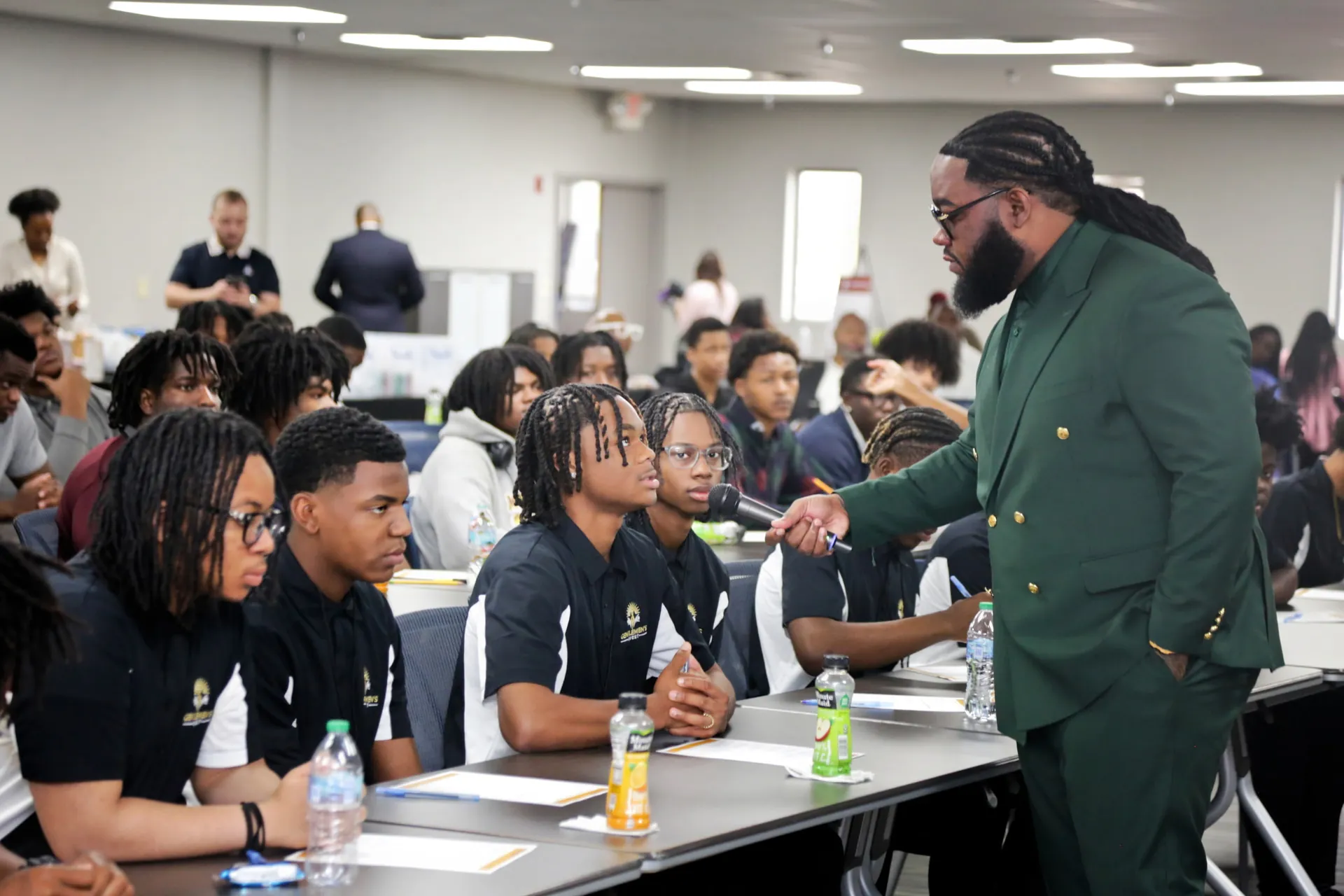 Taj Mahal in a green suit speaking with a microphone to a room of students